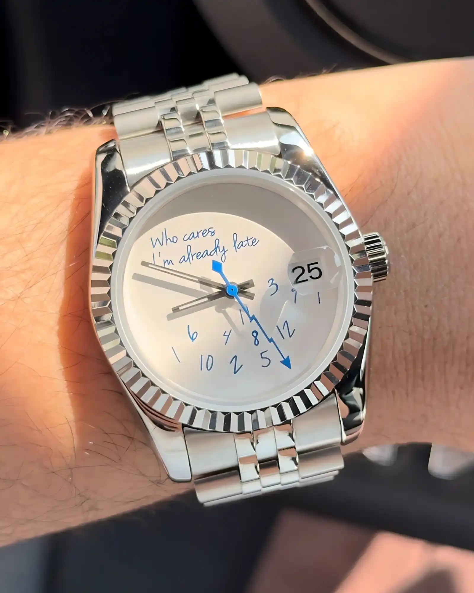 Une montre-bracelet en ton argent avec une lunette cannelée, un cadran blanc et une fenêtre de date.